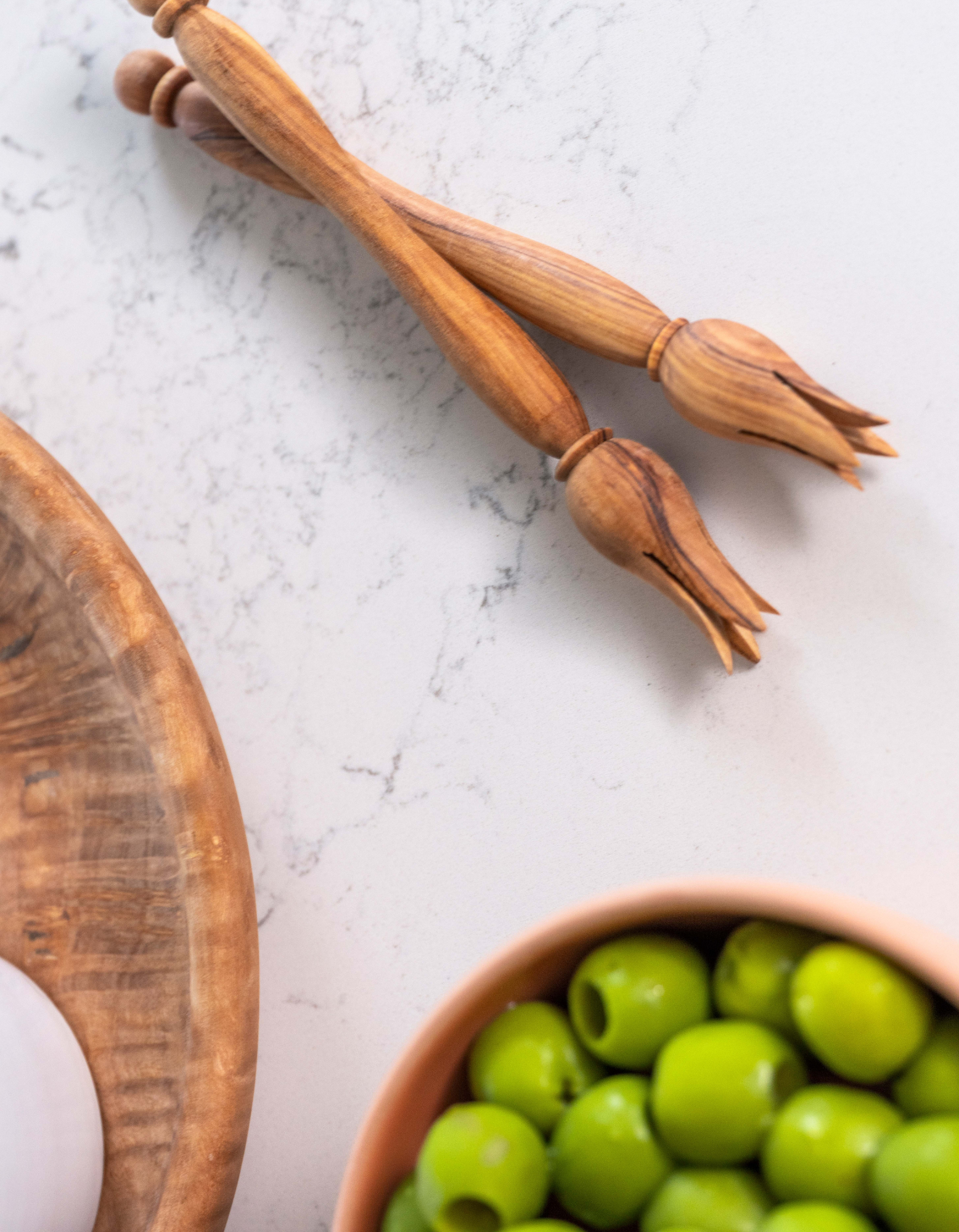 Chad pick olives on marble near a ceramic bowl of olives and olive wood plate Dora