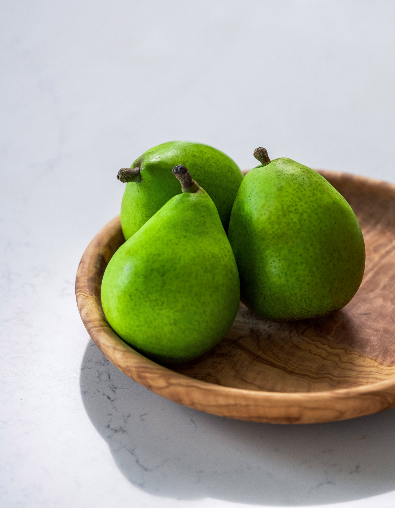 Round olive wood plate handcrafted in Tunisia with three green pears 